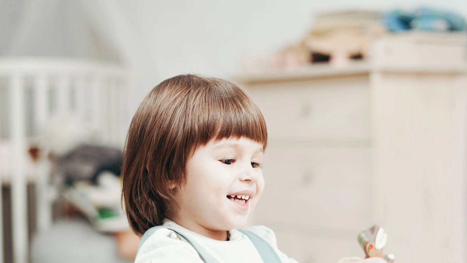Smiling child playing with wooden toy vehicles at a table in a bright room.