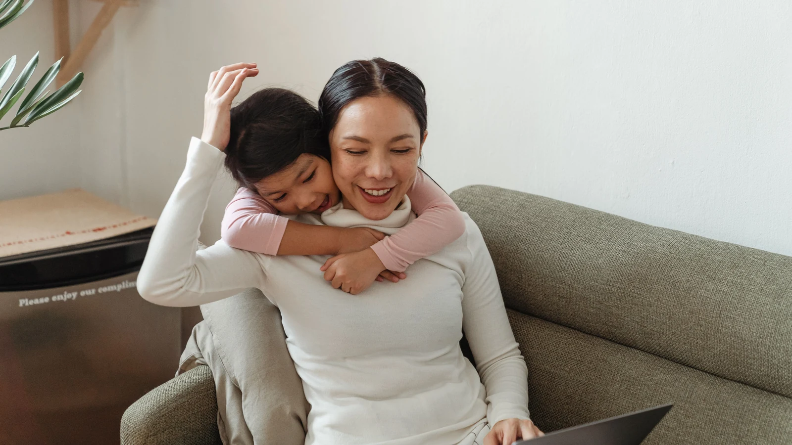 Mother and daughter embracing on a sofa beside a laptop.
